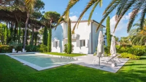 Ampio giardino di villa a Forte dei Marmi con imponente pineta mediterranea e prato verde lussureggiante sotto il sole estivo.